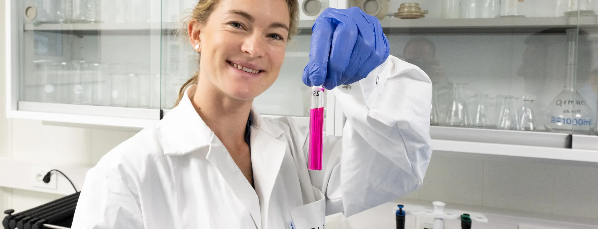 Kvinnelig forsker holder opp reagensrør med rosa væske i laboratorium