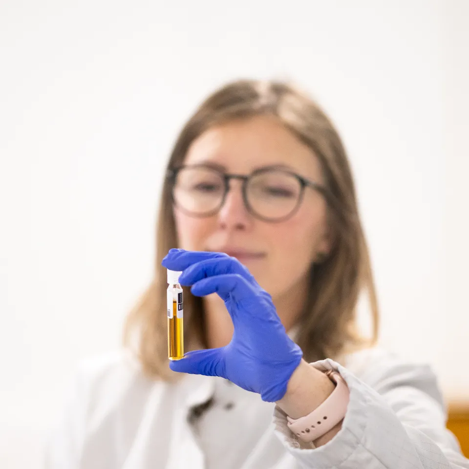 Kvinnelig forsker studerer et glass med gult innhold i Lindums laboratorium