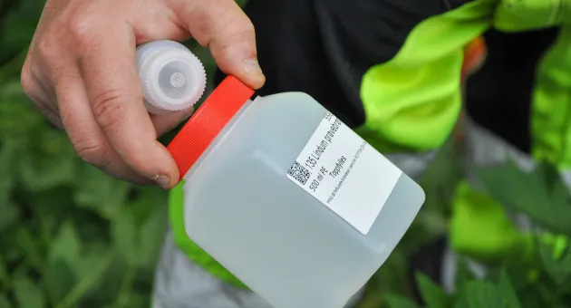 Hånd som holder frem flasker med vann som skal sendes til analyse