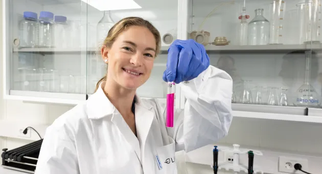 Kvinne i labfrakk viser frem rosa prøver i reagensglass