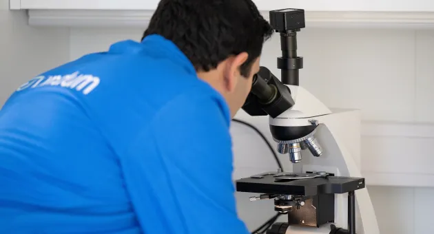 Mann i blå frakk ser inn i mikroskop