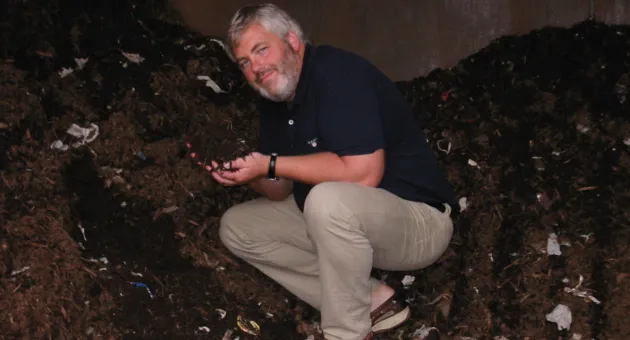 Pål Smits sitter foran komposthaug og holder frem luktfri kompost