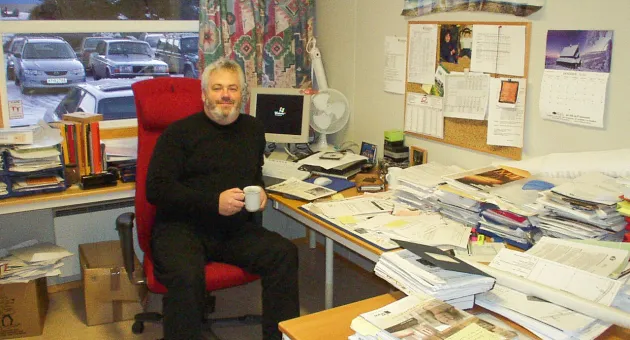 Pål Smits i stol på kontoret omgitt av store papirhauger i brakken som da var administrasjon