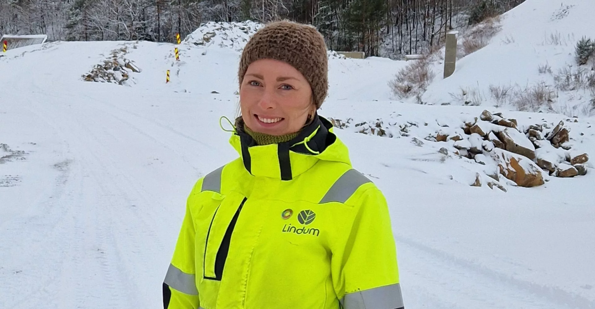 Dame i gul arbeidsjakke og lue med vinter i bakgrunnen